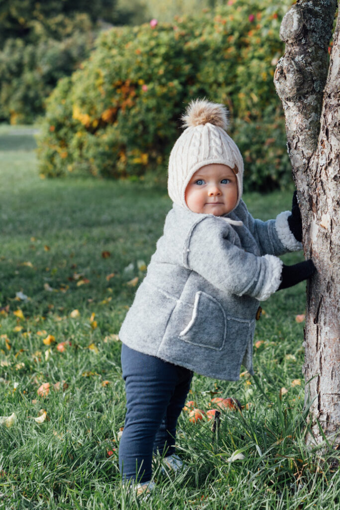 Pieni lapsi seisoo syksyisessä maisemassa ottaen puusta tukea.
